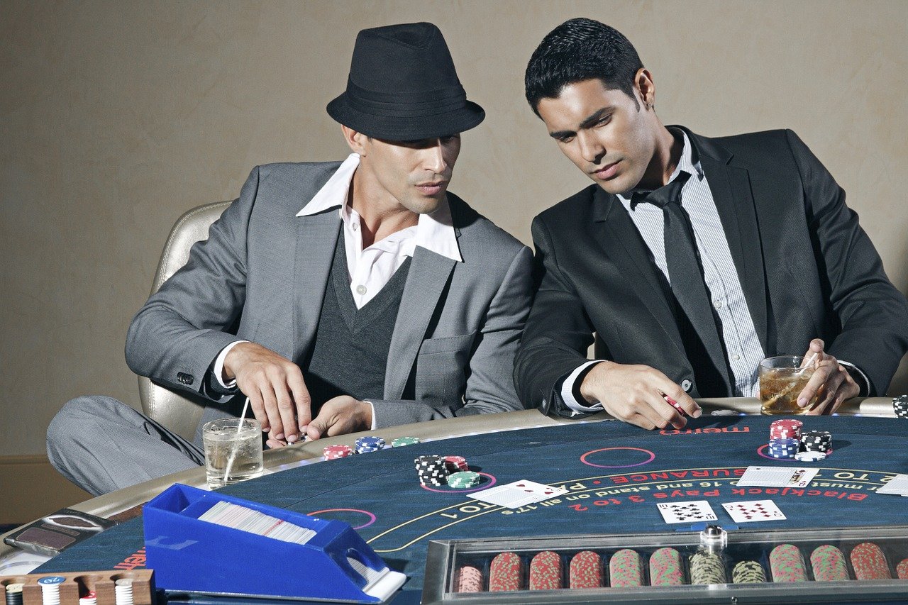 Dois jogadores em mesa de blackjack analisando cartas, fichas e probabilidades do jogo.