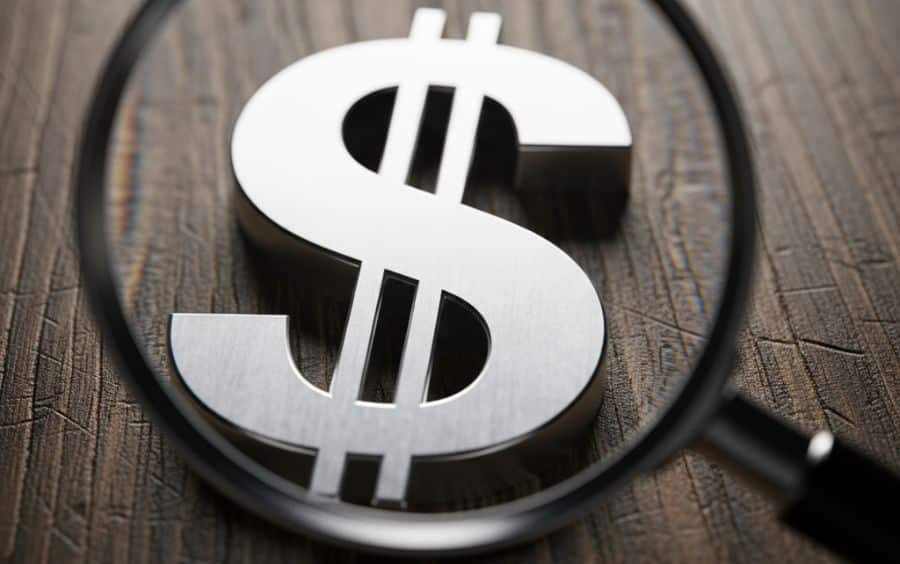 Lupa de aumento focando em um símbolo de cifrão de dinheiro. Ilustra a análise de taxas e custos ao usar Cartão de Débito em Cassinos Online no Brasil, como impostos e tarifas bancárias.