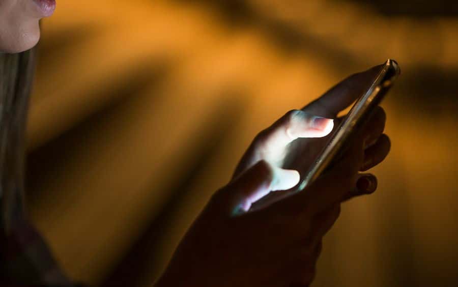 Mão usando celular à noite, sugerindo acesso constante aos jogos online.