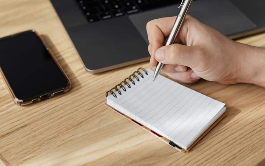 Close-up de uma mão escrevendo dicas de jogo responsável em um caderno, simbolizando o planejamento para jogar apenas por diversão.