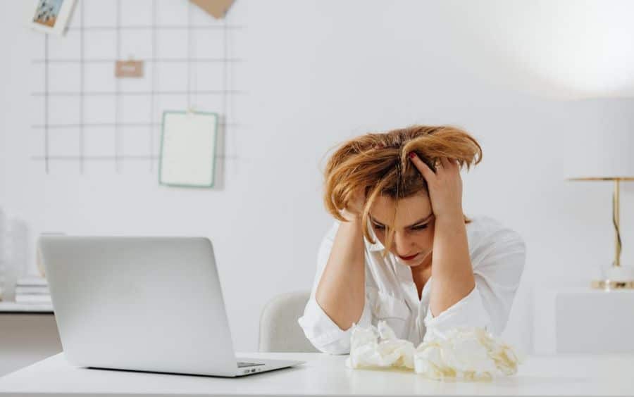 Uma mulher em desespero, com as mãos no cabelo, sentada diante de um laptop. A imagem ilustra o profundo estresse, a ansiedade e o esgotamento causados pelas consequências financeiras e de saúde mental do vício em jogos.