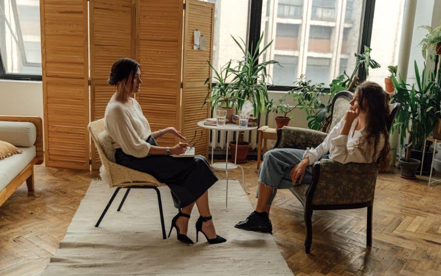 Duas mulheres sentadas em um ambiente acolhedor, uma ouvindo atentamente enquanto a outra compartilha suas experiências sobre vícios. A imagem simboliza apoio, compreensão e a busca por ajuda em grupos de apoio ou atendimento especializado.