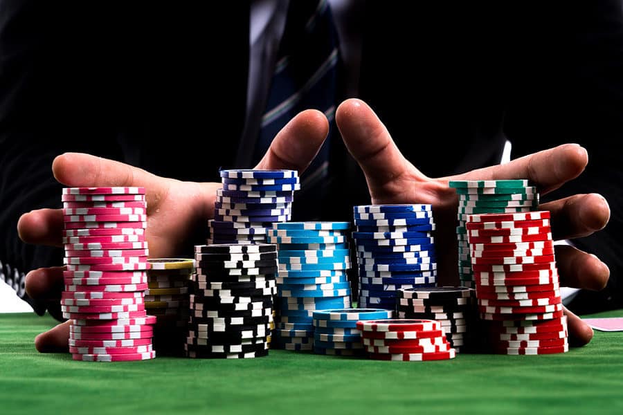 Jogador em mesa de cassino com várias pilhas de fichas, representando apostas altas no blackjack.
